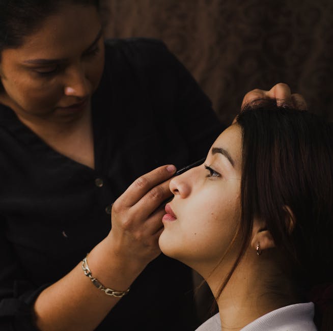 Close-up of a makeup artist meticulously applying eye makeup to a woman indoors.
