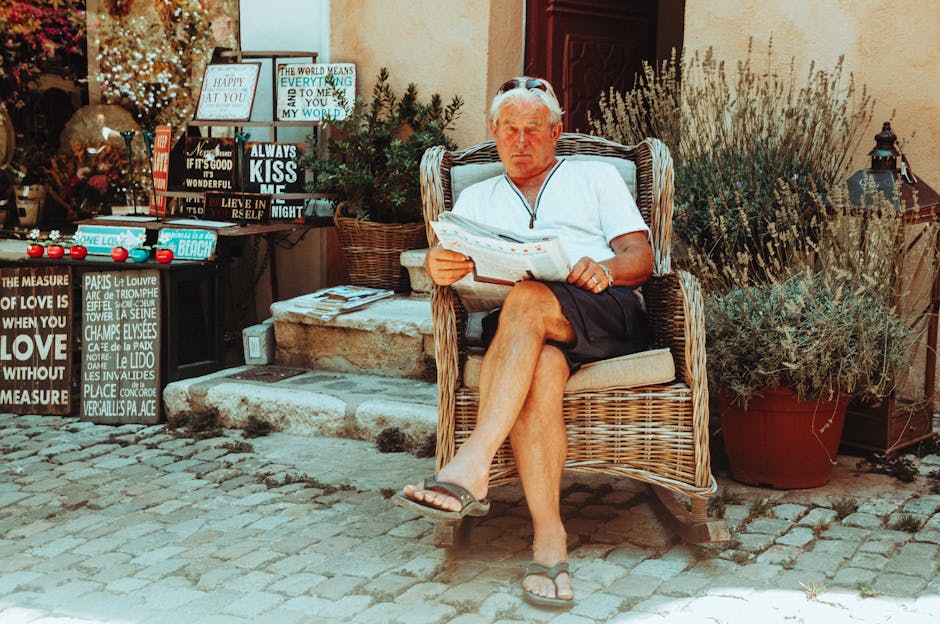 Adult man relaxing in a wicker chair reading a newspaper outside a vintage shop.