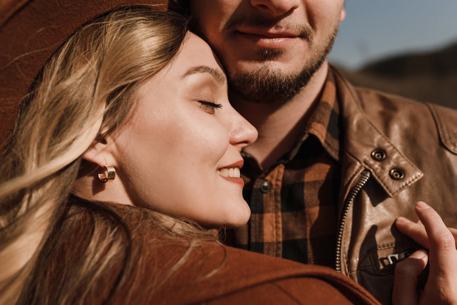 Close-up portrait of a smiling couple embracing in brown leather jackets outdoors.