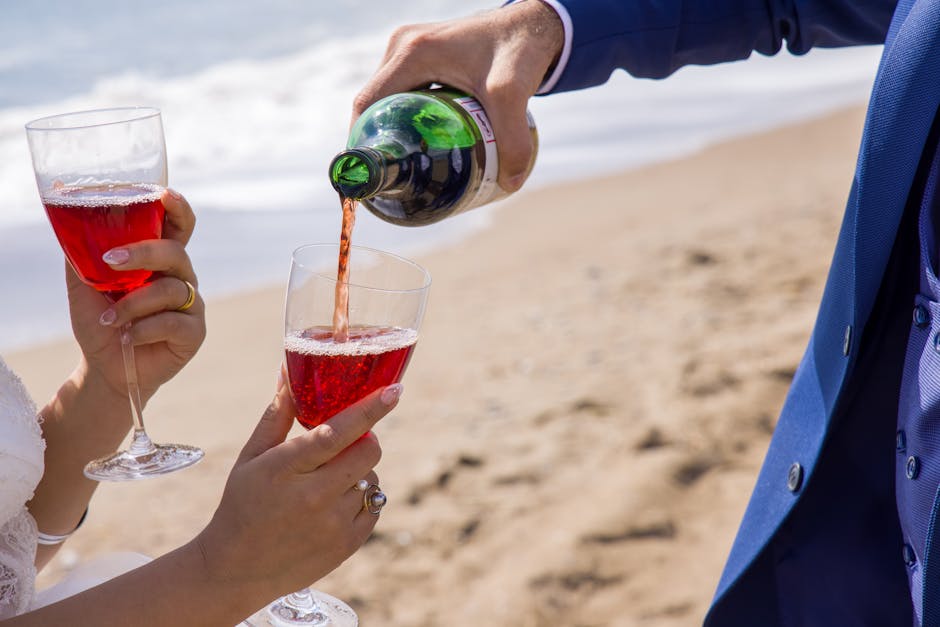 Close-up of red wine being elegantly poured into glasses by the beach.