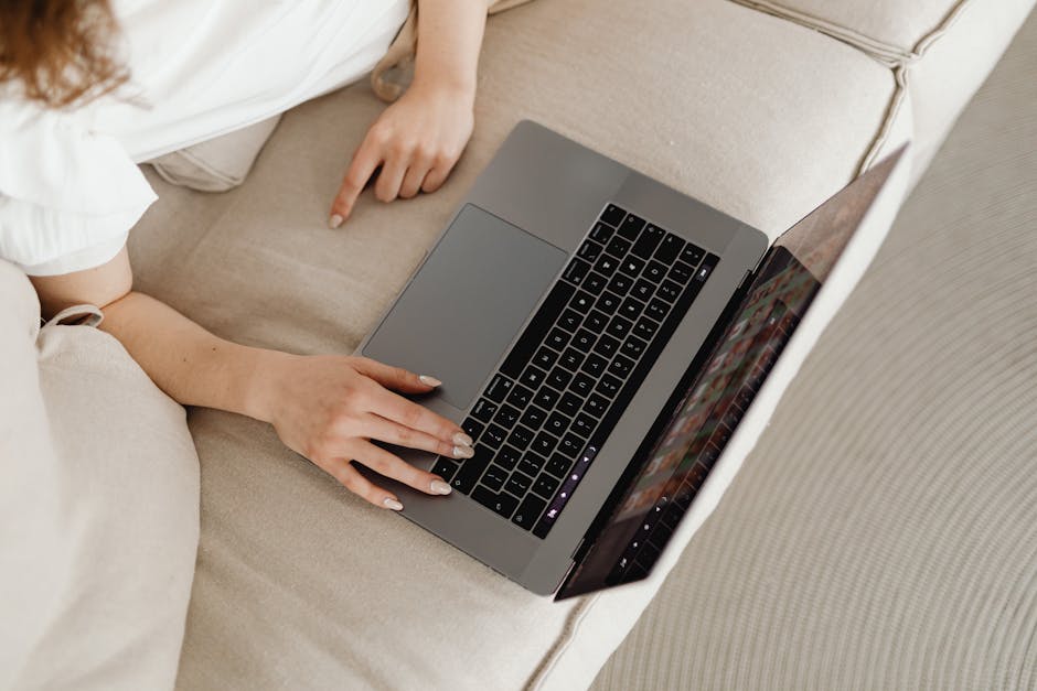 Close-up of a person working from home on a laptop, comfortable on a beige couch.