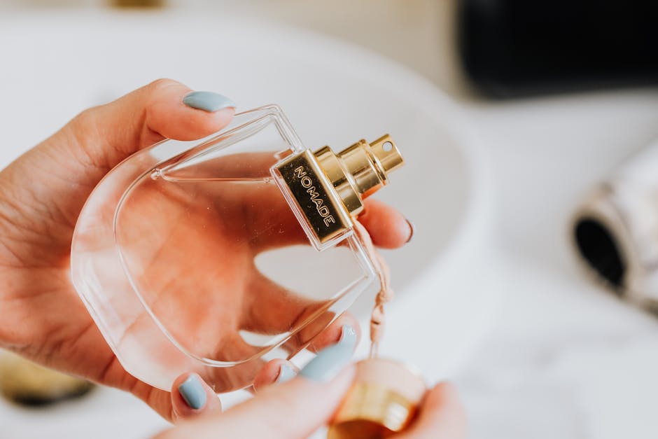 Close-up of a manicured hand holding a clear perfume bottle with a gold cap, emphasizing elegance and fragrance.