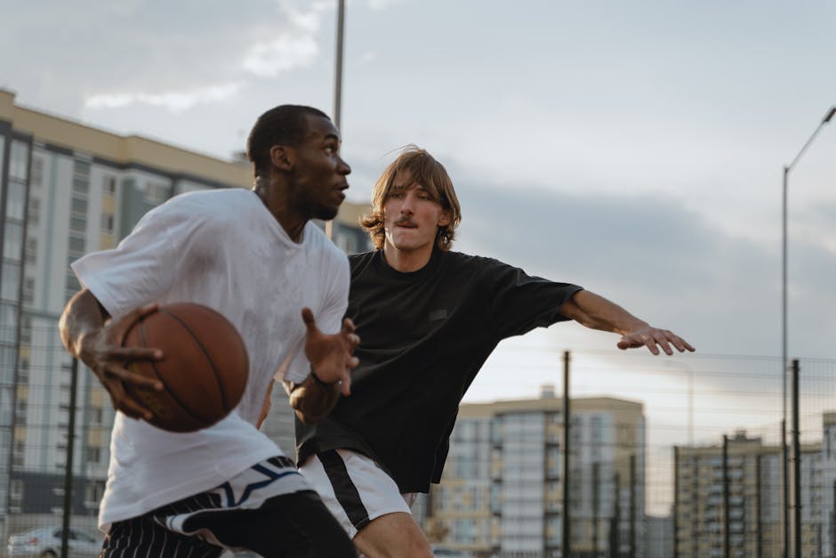 Two men engaging in a competitive basketball match outdoors on an urban court.