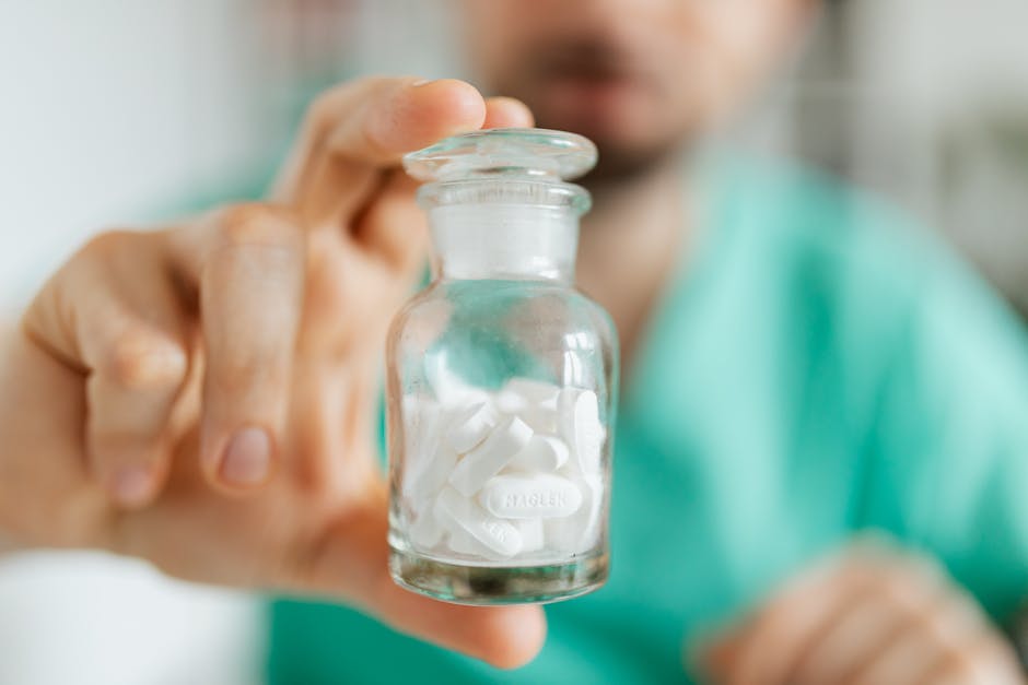 Close-up of a pharmacist holding a transparent glass bottle containing white pills.