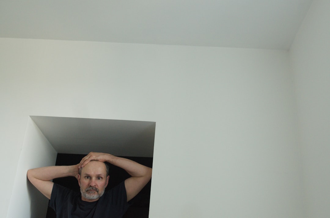 Bald man with hands on head in corner.