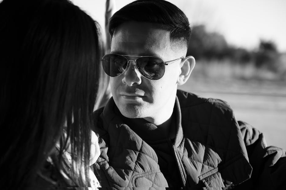 Black and white close-up portrait of a man wearing sunglasses outdoors.