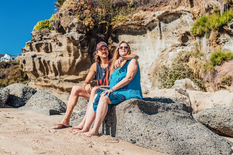 Middle-aged couple enjoying a sunny day on a rocky beach, embracing and smiling.