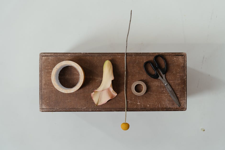 Minimalist flat lay of a calla lily, scissors, and floral tape on wood for crafting.