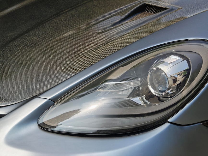 Detailed close-up of a sleek car headlight with a carbon fiber hood, showcasing modern automotive design.