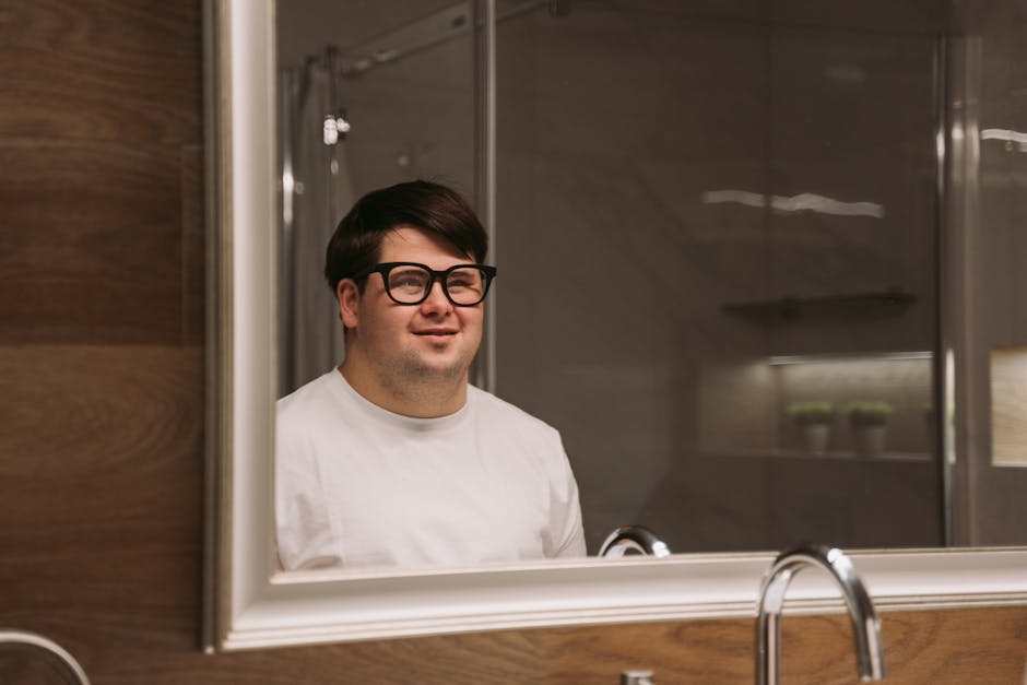 A man wearing glasses smiles at his reflection in the bathroom mirror, creating a warm and inviting atmosphere.