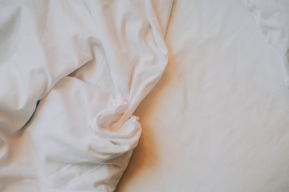 An artistic close-up of crumpled white bed sheets in soft, warm lighting.