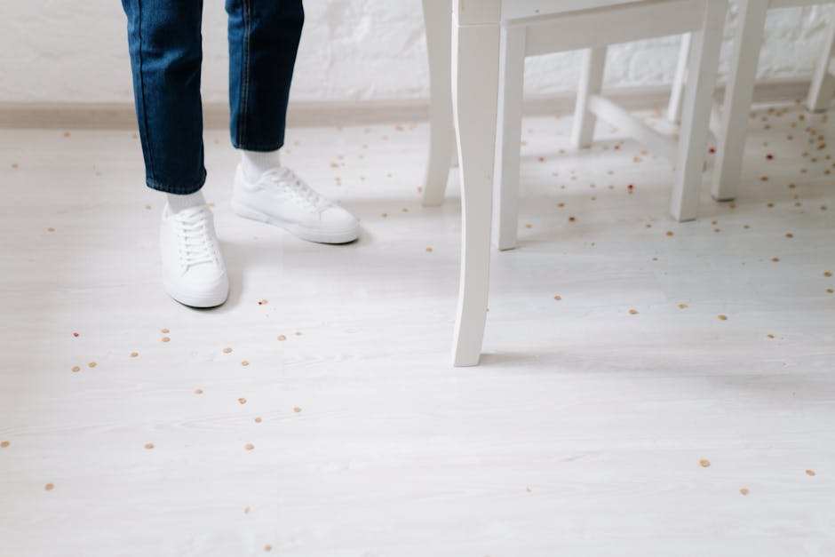 Cornflakes scattered on the floor near a person's legs in a casual indoor setting.
