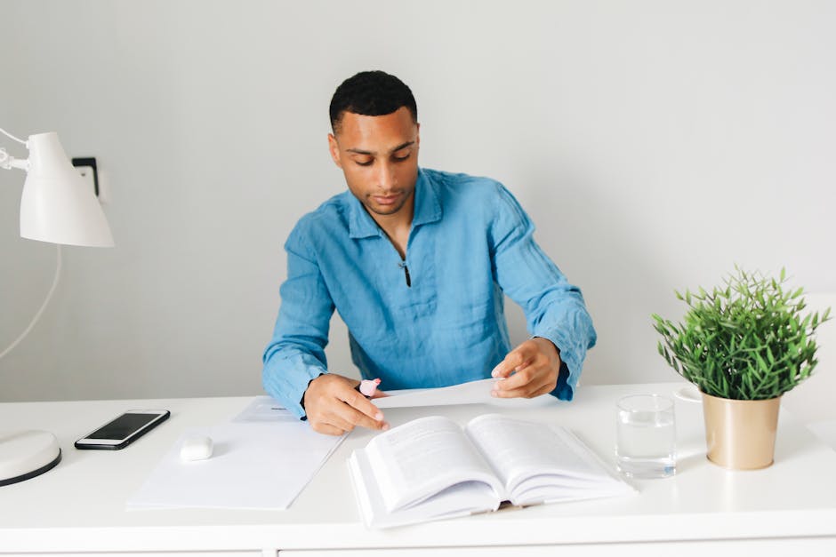 Focused young man reading and studying at a desk with books in a bright home environment.
