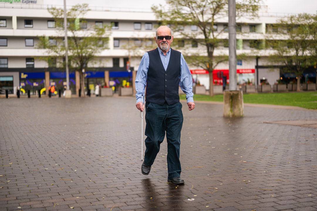 A blind man walks with a white cane outdoors.