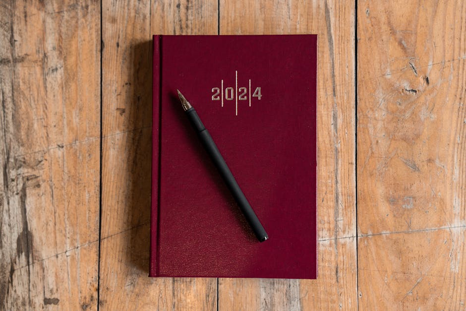 Top view of a red 2024 planner with a pen on a wooden desk surface.